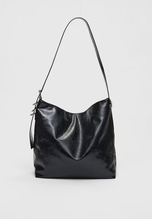Sac à bandoulière en cuir noir brillant avec une seule bandoulière et une forme rectangulaire souple et décontractée sur un fond clair uni.