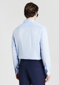 Camicia azzurra a maniche lunghe con una texture liscia, colletto a bottoni e un motivo sottile, abbinata a pantaloni blu scuro e una cintura.