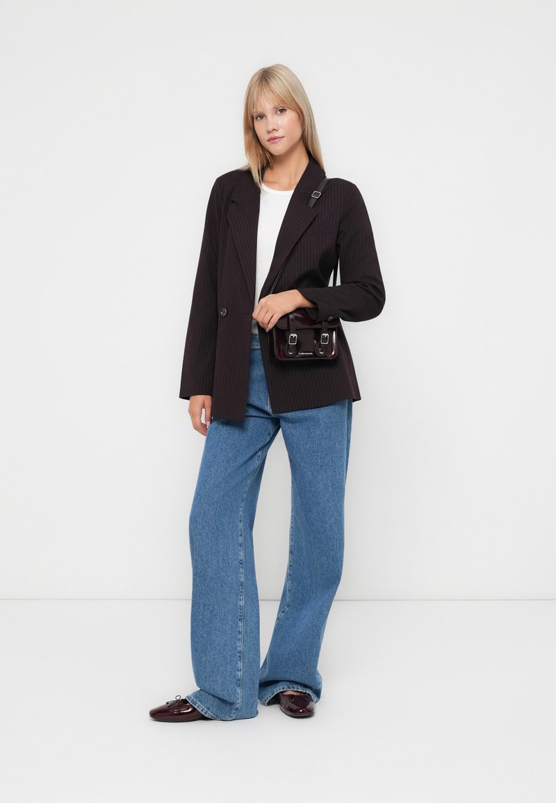 Blazer nero a righe, t-shirt bianca, jeans larghi blu, scarpe bordeaux lucide e una piccola borsa nera con doppi fibbie.