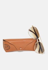 Ochelari de soare Ray-Ban aviatore cu lentile maro cu gradient, ramă din metal aurie și accente negre, alături de un Huse de protecție din piele texturată maro.
