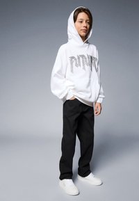 White hooded sweatshirt with "FUTURE" graphic in silver letters, paired with black pants and white sneakers. Simple, casual outfit.