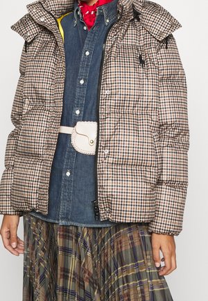 Ruskea ruudullinen untuvatakki farkkupaidan päällä, valkoinen vyölaukku, punainen kaulahuivi ja monivärinen ruudullinen laskostettu hame.