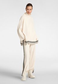 Conjunto de loungewear color crema que incluye una camiseta de cuello alto y pantalones de pierna ancha, acentuado con rayas negras en el dobladillo y las costuras laterales.