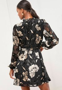 Rochie neagră cu model floral, dintr-un material transparent, având motive florale aurii și detalii subtile cu mărgele. Mâneci lungi și decolteu plisat adaugă eleganță.