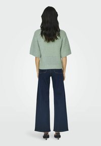 Top a maglia verde chiaro con un motivo testurizzato, maniche larghe corte, abbinato a jeans a gamba larga blu scuro e sandali neri con tacco.