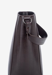 Brun læderhåndtaske med en konisk form, der har lodrette striber, en topåbning, metalbeslag og en justerbar skulderrem.