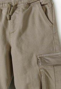 Beige cargobroek van een zachte, duurzame stof, met een elastische tailleband met trekkoord en een zijvak voor extra functionaliteit.