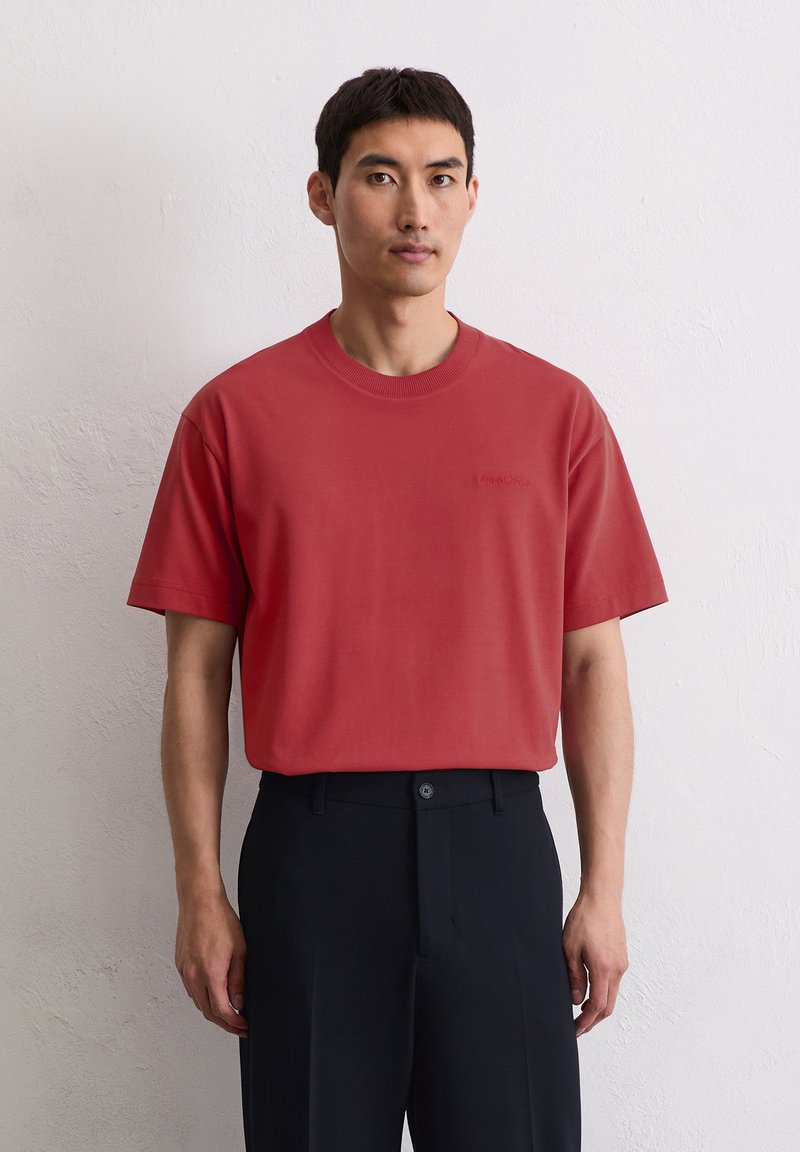 Czerwona bawełniana koszulka z krótkim rękawem i okrągłym dekoltem, z subtelnie haftowanym logo na piersi, zestawiona z czarnymi spodniami.