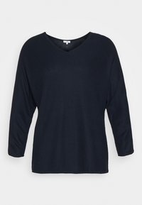 Marinblå långärmad topp med V-ringning, tillverkad av textilier med en subtil zigzag-mönster. Avslappnad passform och rak fåll.