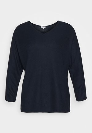 Haut bleu marine à manches longues avec un décolleté en V, fabriqué en tissu texturé arborant un motif zigzag subtil. Coupe décontractée et ourlet droit.