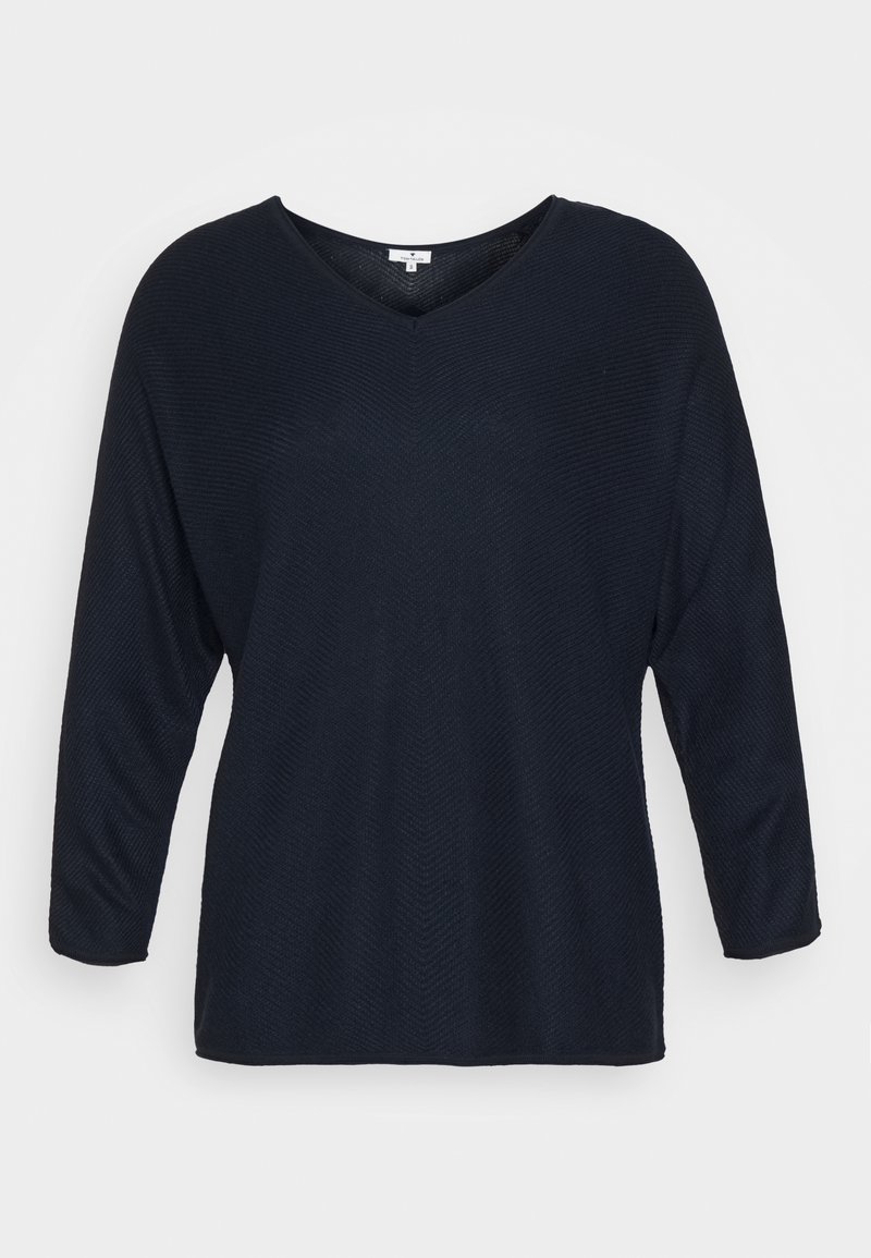 Marinblå långärmad topp med V-ringning, tillverkad av textilier med en subtil zigzag-mönster. Avslappnad passform och rak fåll.