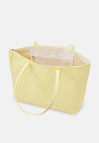 Gul toteväska med en slät, matt yta. Två handtag, dragkedjestängning och inre fack. Minimalistisk design med ett lätt och luftigt utseende.