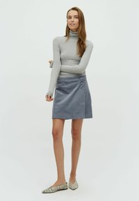 Pelēkas turtleneck krekliņš, apvienots ar zilu korduroja svārku, kuram ir trīs lieli pogas vienā pusē un norādītas, ar rakstu rotātas kurpes.