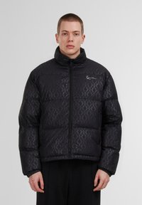 Giacca a vento nera con un motivo sottile, colletto alto, zip anteriore e polsini elasticizzati. Realizzata in materiale resistente all'acqua con un design trapuntato.
