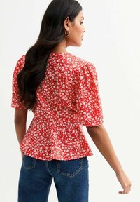 Red floral blouse with short puff sleeves, cinched waist, and a peplum hem; made of lightweight fabric featuring small white flowers.