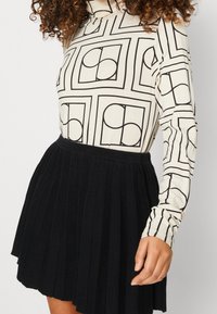 Långärmad topp med en krämfärgad bakgrund och svarta geometriska mönster, tillsammans med en plisserad svart kjol i ribbad tyg.