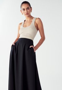 Bež ribana top brez rokavov v kombinaciji z črnimi, širokimi krilom do gležnjev, ki ima stranske žepke in prilagojen pas.