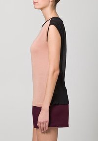 Short-sleeve top with a light pink front and sheer black back, featuring a relaxed fit and smooth texture, paired with maroon shorts.