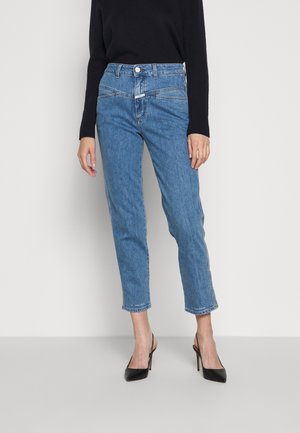 Jean en denim bleu clair avec une taille haute, une coupe droite, un ourlet brut et des détails subtils de couture à l'avant. Porté avec des talons hauts noirs.