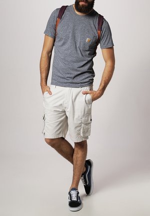 Grau meliertes T-Shirt mit einer Brusttasche, beige Cargo-Shorts mit Seitentaschen und schwarz-graue Sneakers. Braune Rucksackriemen sind sichtbar.
