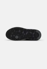 Suola di scarpa nera con superficie testurizzata caratterizzata da motivi circolari di diverse dimensioni. I segni indicano "GEOX" e la tecnologia traspirante.