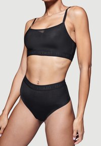 Schwarzes Spitzenunterwäsche-Set mit einem schlichten Bralette mit dünnen Trägern und hochgeschnittenen Shorts. Glatte Textur mit einem Logo-Band am Bund.