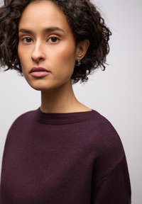 Breipullover in donkerpaars, ronde hals, gestructureerde stof, met een losse pasvorm en verlaagde schouders. Eenvoudig ontwerp, zonder zichtbare patronen.
