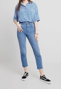 Blå skjorta med prickar och korta ärmar samt krage, som matchas med högmidjade ljusblåjeans och svarta sneakers med vita sålar.