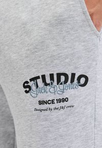Szara bluza z dużym nadrukiem graficznym z tekstem "STUDIO Jack & Jones" w czerni i jasnoniebieskim, obok "SINCE 1990."