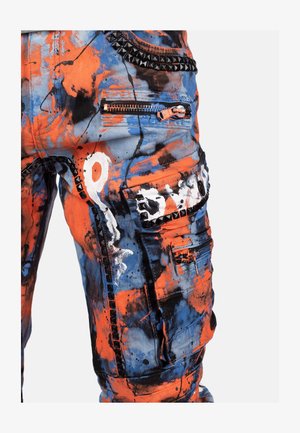 Stof broek met een combinatie van oranje, blauwe en zwarte spetterpatronen. Inclusief ritszakken en zwarte studs langs de naden.