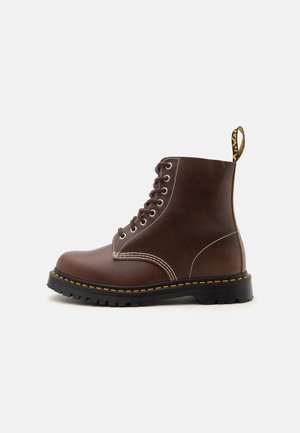 Bruine leren veterboot met zwarte dikke zool en gele stiksels, zijaanzicht, met trekkerslus aan de achterkant.