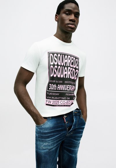 Weißes T-Shirt mit großen schwarzen und rosa grafischen Text, kombiniert mit blauen Jeans aus Denim mit einem distressed Finish und einzigartigen Knopfdetails.