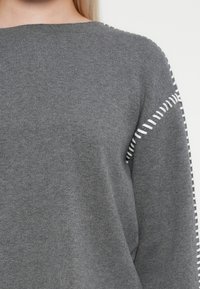 Gray knitted sweater featuring a round neckline, distinct texture, and white stitched accents along the shoulder seams.