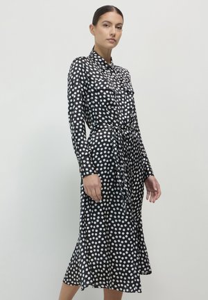 Black dress with white polka dots, long sleeves, button-up front, two chest pockets, belted waist, and a flared hemline. Smooth texture.