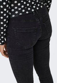 Jeans de mezclilla oscura con corte ajustado, que cuentan con dos bolsillos traseros y costuras sutiles. Se llevan con una blusa de lunares en blanco y negro.