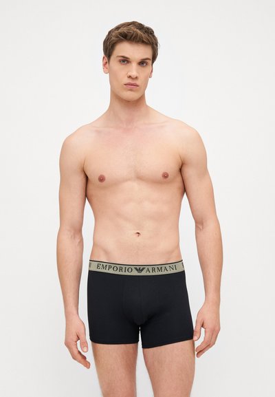 Juodi medvilniniai bokseriai su prigludusia forma, su smėlėnos spalvos elastine juosta, ant kurios parašyta "EMPORIO ARMANI".