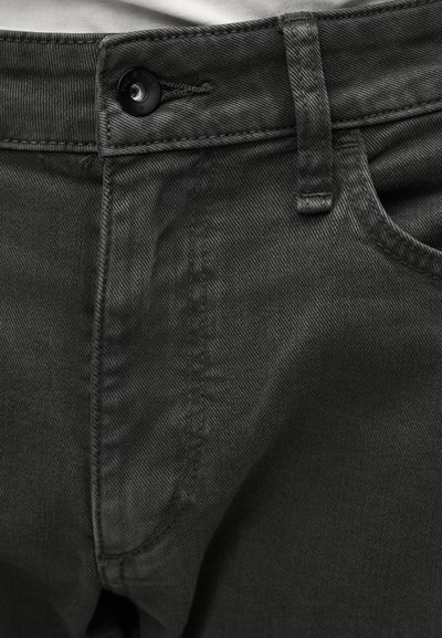 Τα τζιν σε σκούρο γκρι έχουν κούμπωμα με κουμπιά, φαρδύ ζωνάρι και εμφανείς ραφές. Το ύφασμα έχει λεπτή υφή.