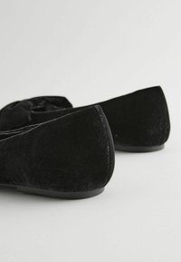 Svarta mocka ballerina skor med rund tå, en liten rosettdetalj på framsidan och en elegant låg klack. Slät textur och minimalistisk design.