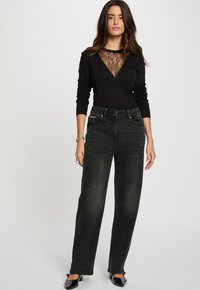 Sweater noir à empiècements en dentelle avec un décolleté en V associé à un jean noir taille haute. Les deux pièces présentent une coupe slim et des détails minimalistes.