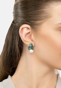Green floral-shaped earrings with textured petals accented by small green stones and a white pearl drop detail.
