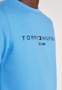 Felpa azzurra chiara realizzata in tessuto morbido. Presenta un collo rotondo, testo ricamato "TOMMY HILFIGER" con logo e polsini a coste.