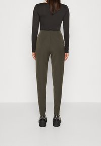 Fitted olivgröna byxor med en slät textur, hög midja och avsmalnande ben, i kombination med svarta plattformsskor.
