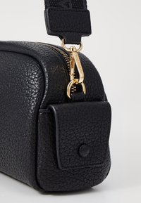 Svart läder crossbody-väska med en texturerad yta, gulddragkedja och en framficka med kläppen som har ett tryckknappslås. Justerbar rem ingår.