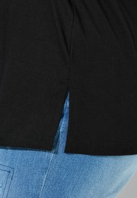 Schwarzes Baumwoll-T-Shirt mit Seitenschlitzen, kombiniert mit blauen Denim-Jeans. Verfügt über eine glatte Textur und eine lockere Passform.