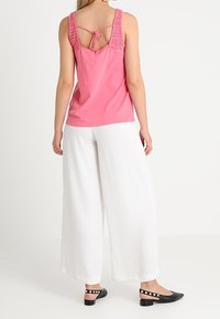 Rosa tanktop med blonder accented stropper, med en knyttet ryg. Matchet med brede hvide bukser og sorte flade sko med hvide prikker.