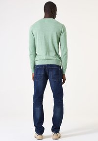 Lichtgroene trui met geribde halslijn en manchetten, gecombineerd met donkerblauwe jeans. De jeans hebben achterzakken en een slim fit ontwerp.