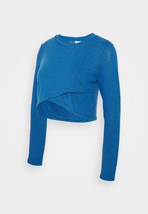 Haut court à manches longues bleu en tissu doux et texturé ; présente un design asymétrique à l'avant et un col rond.