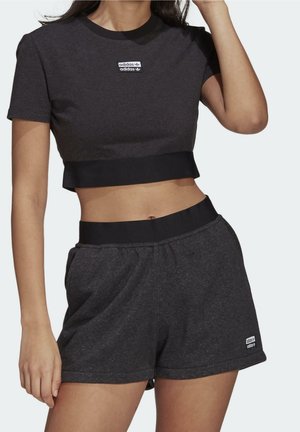 Woman wearing dark gray Adidas crop top and matching shorts with black waistbands and Adidas logo patches on chest and thigh.