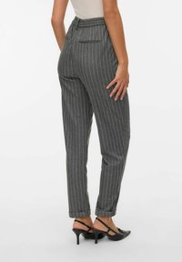 Szare spodnie w paski o luźnym kroju, elastycznym pasku w talii i mankietach. Tkanina wydaje się gładka; zawiera detal w postaci tylnej kieszeni.