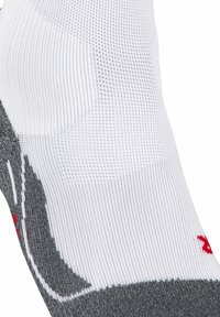 Calcetín atlético blanco y gris con textura acanalada, que presenta un acento gris y un logo rojo. Primer plano que muestra el patrón de tejido y el diseño ajustado.
